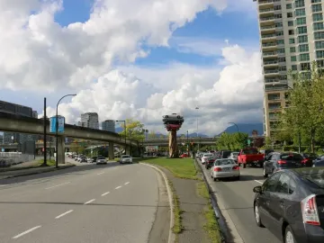 Trans Am Rapture sculpture with stacked cars mounted on a tall stripped tree trunk in Vancouver, framed by high-rise buildings.