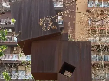 El Llarg Viatge, a tall rust-colored abstract metal sculpture with a square cutout on a brick platform.