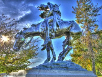 End of the Trail bronze sculpture of a bowed rider on a weary horse against a blue sky.
