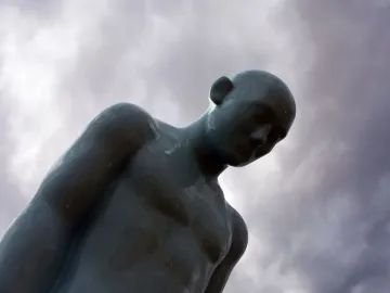 Greetingman sculpture with a bowed head against a cloudy sky.