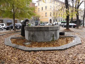 Saint Francis Fountain beside a basin covered with fallen autumn leaves, with a robed statue holding a red rose.