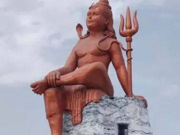 The Statue of Belief, a massive seated Shiva statue with a cobra and trident on a large base under a cloudy sky.
