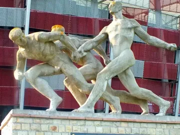 Sztafeta sculpture showing three nude male figures passing a baton on a stone base.