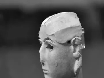Warka Mask shown in profile on a dark stand, with hollowed eyes and an incomplete top and back.