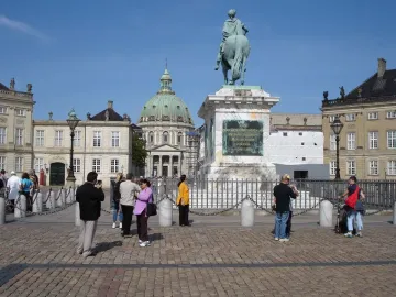 Frederick V equestrian statue on a tall marble pedestal in a sunny square, with people nearby and a green-domed church in the background.