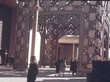 Ornate architectural tower interior with decorative latticework and panels, with people walking below.