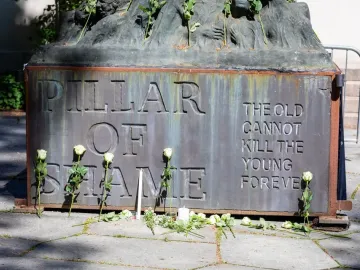 The Pillar of Shame base with white roses and candles arranged around the memorial inscription.