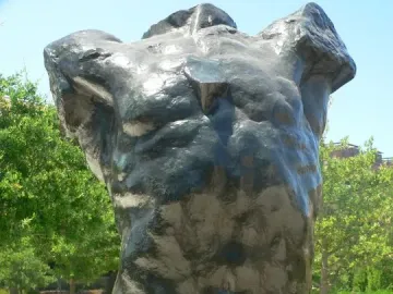 The Falling Man bronze torso sculpture on a concrete plinth in a park setting.