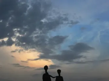 Silhouette of the Monument to the Victims of Fascism showing two adults and a child against a twilight sky, with water and trees behind it.