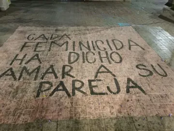 Painted Spanish text on a tiled surface at The Roundabout of the Disappeared reads “Cada feminicida ha dicho amar a su pareja.”