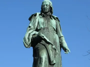 The Vodnik Monument shows a weathered green statue of a man in a long robe holding a rolled document on a stone pedestal.