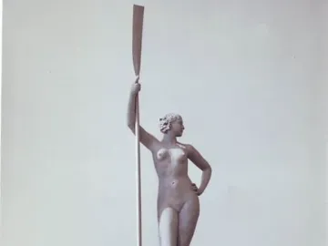 Girl with an Oar sculpture standing on a tiered pedestal in a park fountain, holding a tall oar upright.