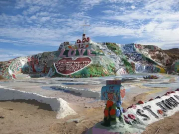 Salvation Mountain with colorful painted stripes, large hearts, religious messages, and a white cross on top.