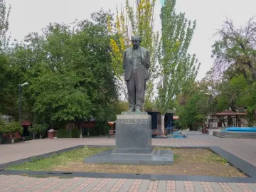 Monument to Avetik Isahakyan in a tree-lined public square with benches and small kiosks nearby