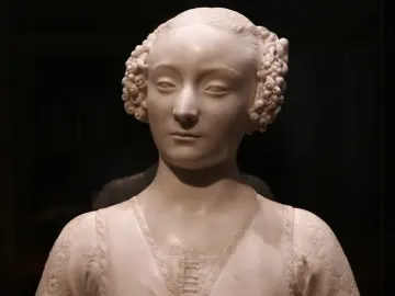 Marble bust of a young woman with tightly curled hair and an ornate carved garment.