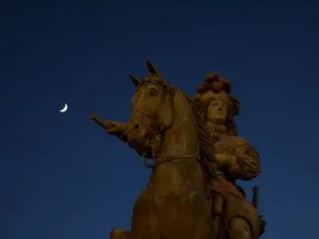 The Equestrian Statue of Louis XIV silhouetted against a deep blue evening sky with a crescent moon above.