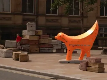 Superlambanana sculpture beside stacks of old suitcases on a paved outdoor area, with a child in the background.