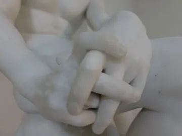 Clasped marble hands from The Exiled, with part of the figure’s arms and torso visible.