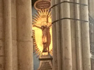 Gero Cross crucifix with Christ before a golden sunburst, framed by stone columns.