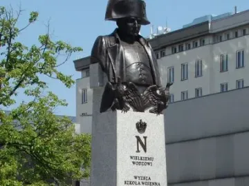 Bronze bust of Napoleon I on a tall stone plinth with engraved symbols and wreaths at the base.
