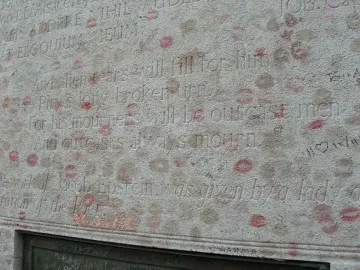 Inscribed stone section of Oscar Wilde\'s tomb covered with lipstick kiss marks and graffiti.