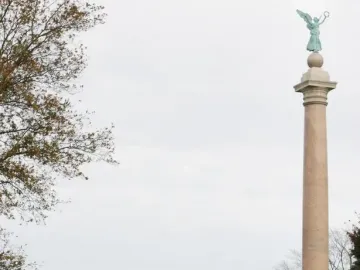 Battle Monument at West Point with soldiers marching past it beside the Hudson River.