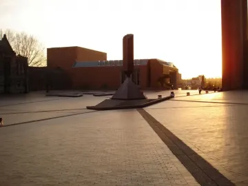 Broken Obelisk sculpture in a paved plaza with brick buildings in the background.