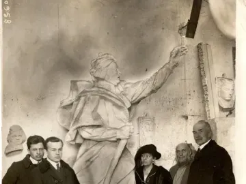 A group of five people stands around a large sculpture of Mickiewicz in a workshop, with other busts and reliefs on the walls.