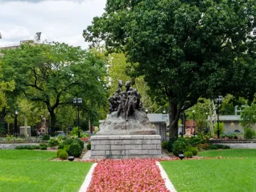 Wars of America bronze sculpture on a stone base in a green park with trees and a flower-lined path.