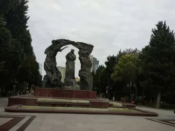 Huseyn Javid Monument with a central robed figure holding a staff, set on a stone base in a park.