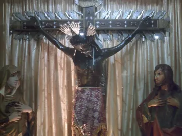San Juan Patrón crucifix with a dark-skinned Christ statue, flanked by a veiled woman and a bearded man.