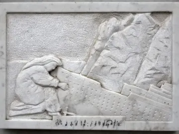 Detail of the Titanic Musicians\' Memorial showing a white marble relief of a kneeling figure reaching toward a listing ship, with musical notation below.