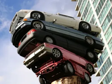 Trans Am Rapture sculpture with cars stacked vertically against a blue sky and a high-rise building.