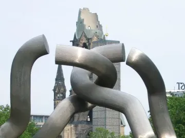 Brushed metal sculpture with interlinked tubular segments in front of the Gedachtniskirche tower.