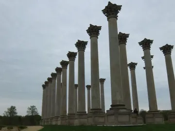 Capitol Columns standing in rows on a grassy lawn with a winding path and trees under a cloudy sky.