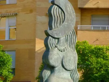 Dona Lluna bronze sculpture of a stylized female figure with a crescent moon above her head on a yellow patterned pedestal.