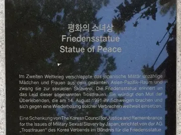 Informational plaque for the Statue of Peace with Korean, German, and English text on a stone base.