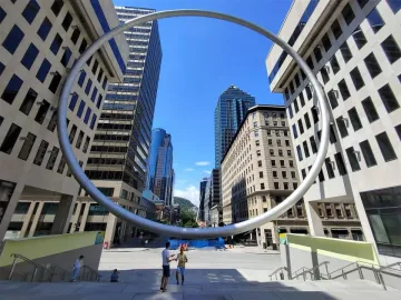 The Ring sculpture framing a city street and plaza under a bright blue sky.