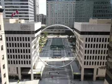 The Ring, a large circular sculpture suspended above an urban plaza between two buildings.