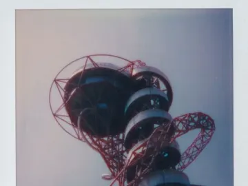 Orbit Tower’s red lattice structure with dark spiral observation decks against a pale sky.