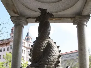 Bronze fish sculpture on the Temperance Fountain, framed by two stone columns with buildings in the background.