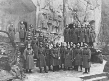 Soldiers posed on steps below the Externsteine Relief carved into the rock face.