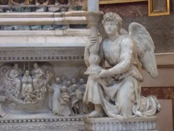 Michelangelo\'s Angel kneeling and holding an ornate candelabra beside carved marble relief.