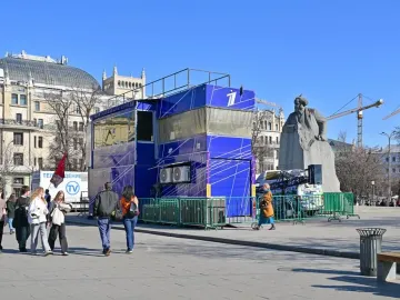 Monument to Karl Marx in a public square, partly obscured by a blue structure and green barriers.