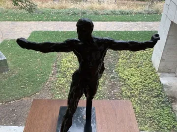 Standing Mercury, a dark bronze nude male sculpture posed with one leg lifted and both arms extended.