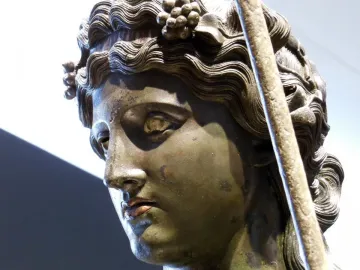 Close-up of the bronze head of Tiber Dionysus with wavy hair, a grape wreath, and inlaid eyes.