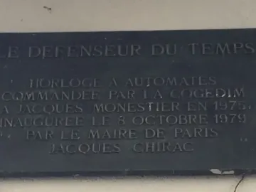 Plaque for Le Défenseur du temps with engraved French text on a dark rectangular panel.