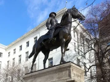 Joseph Hooker equestrian statue on a tall stone pedestal with HOOKER inscribed on the base, set against buildings and blooming trees.