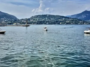Life Electric sculpture rising from a pier on Lake Como, with mountains and lakeside towns in the distance.