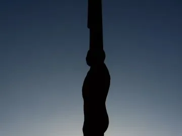The Angel of the North silhouetted against a bright sky, with small figures near its base.
